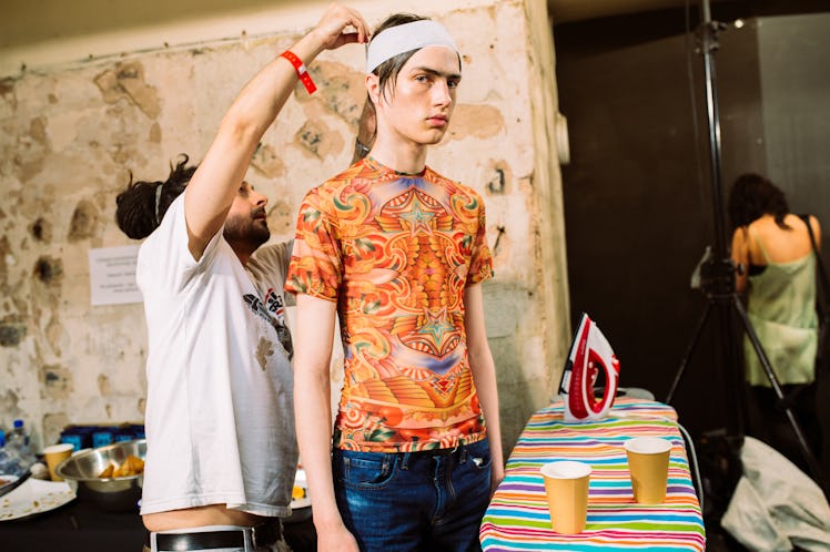 A designer putting a white headband on the head of a model that is wearing an orange shirt