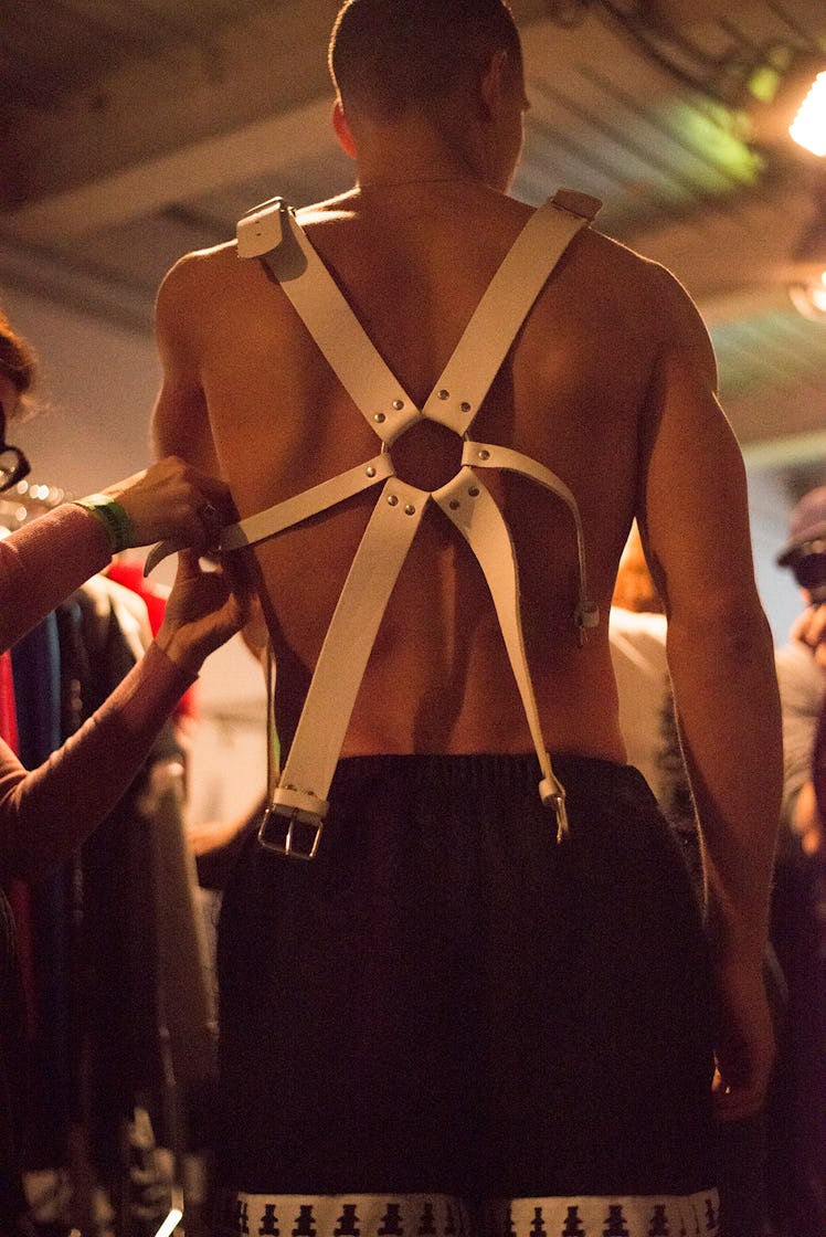 A stylist attaching harness on a male model backstage at London Fashion Week