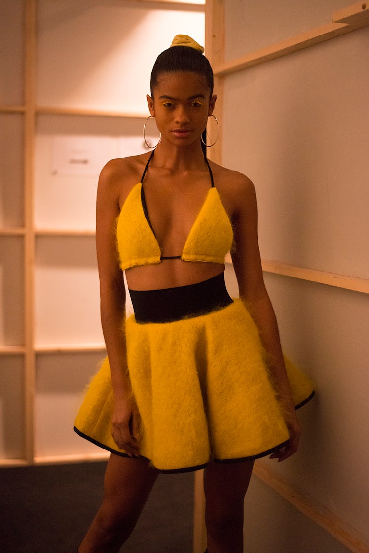 A model wearing a yellow bralette and a matching skirt backstage at London Fashion Week