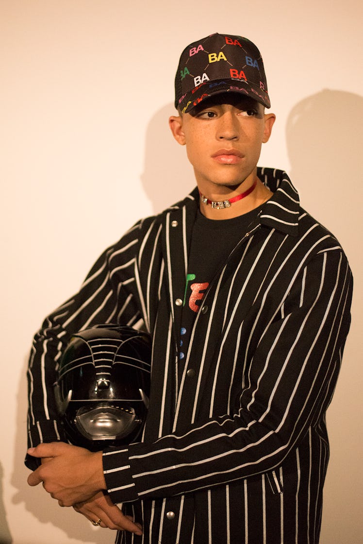 A model in Bobby Abley outfit, holding a black Power Ranger helmet backstage at London Fashion Week