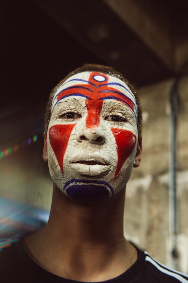 A male model standing while having a red and white drawing on his face