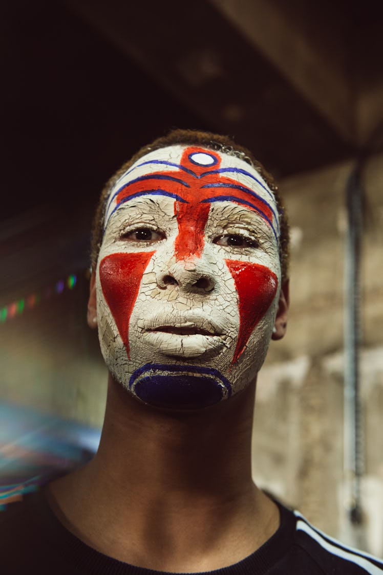 A male model standing while having a red and white drawing on his face