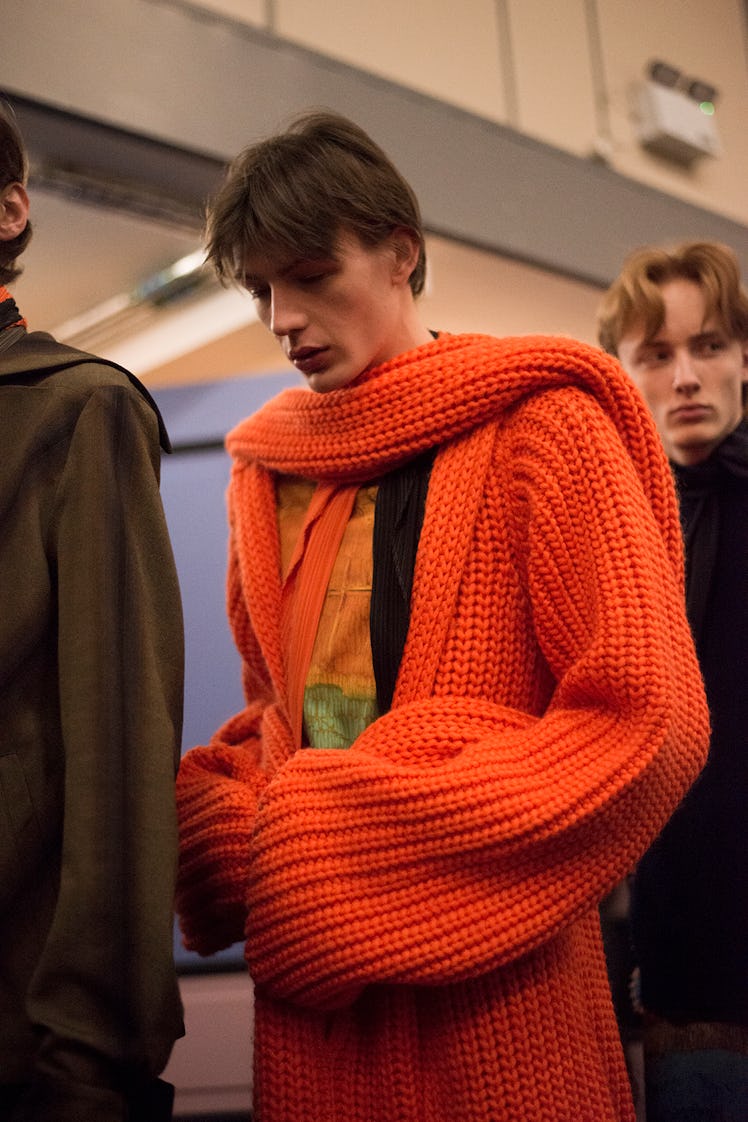 A model backstage wearing an orange knit coat from J.W. Anderson’s Fall/Winter 2017 Collection.
