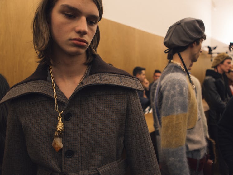 A model in a brown jacket standing next to other models backstage at Prada's Fall 2017 Collection