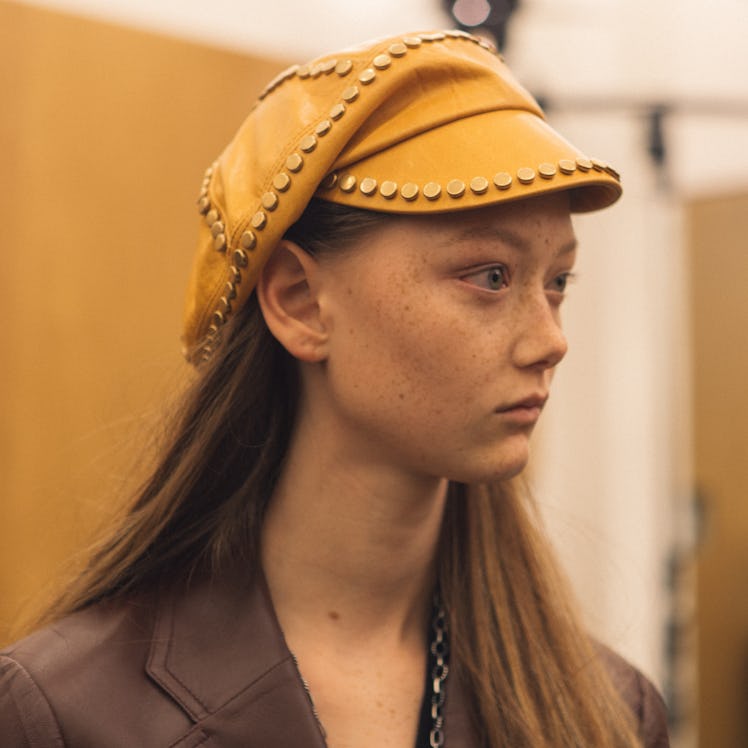 A close-up of a model with a yellow hat backstage at the Fall 2017 Prada Fashion Show