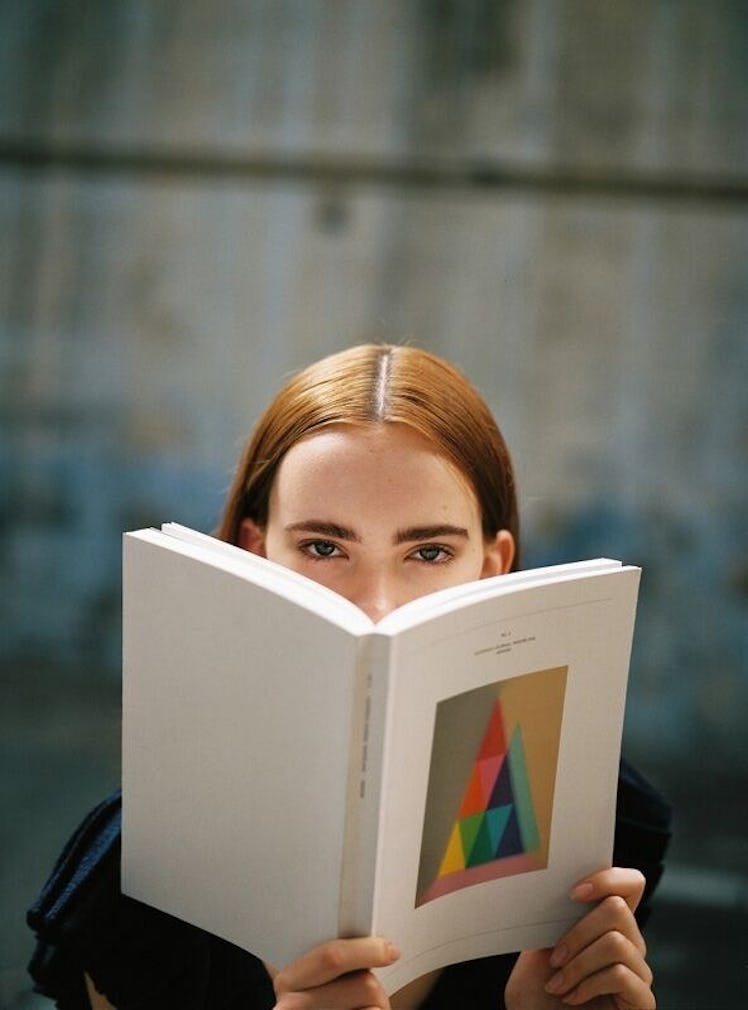 A model wearing a black top while reading a book, covering most of her face, from the Hesperios Spri...