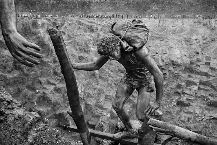 A man carrying a bag on his back and holding onto a stick in Serra Pelada opencast gold mine, Para, ...