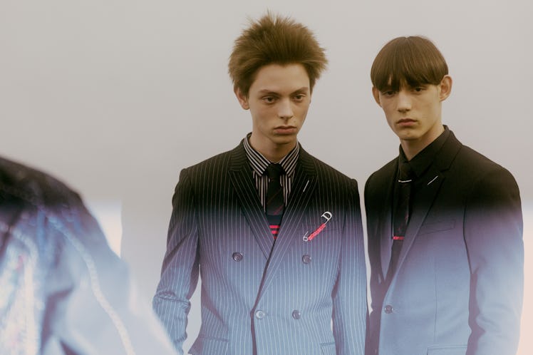 Two models in black Dior blazers with stripes standing backstage at the show, looking into the dista...