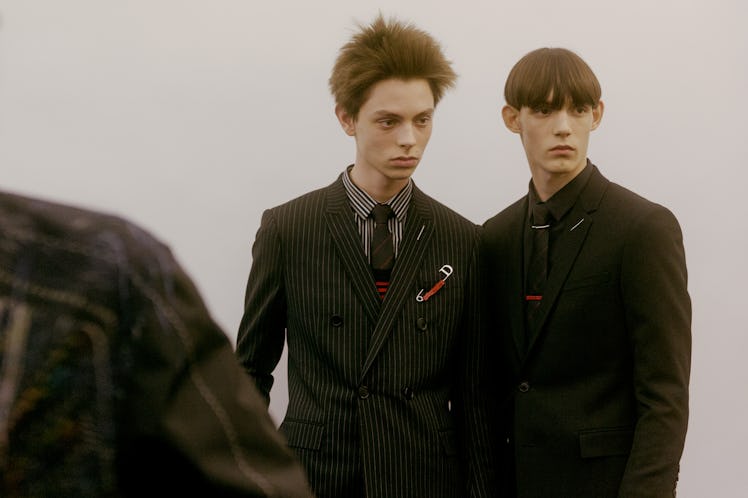 Two models backstage at the Dior Homme Fall 2017 show in black suits looking into the distance 