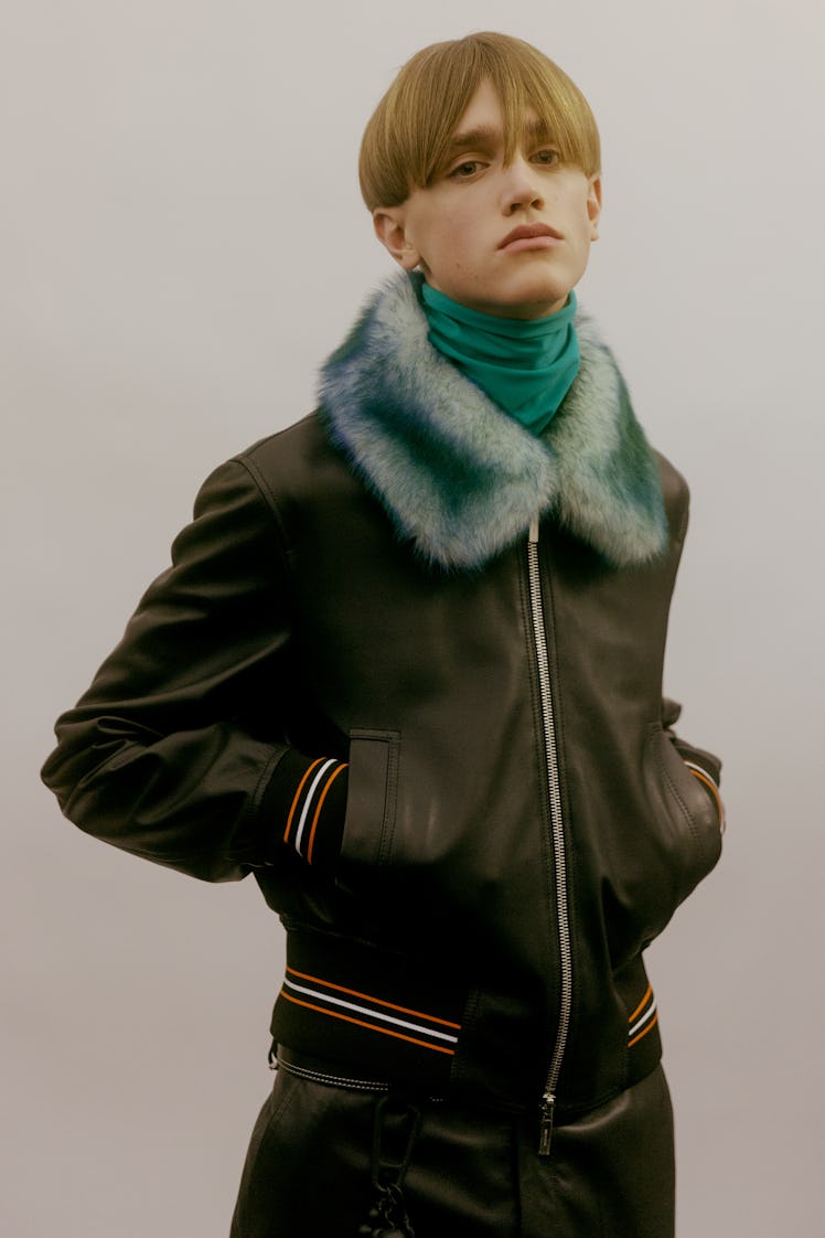 A model posing at the Dior Homme Fall 2017 show in a black leather jacket with a light blue fur coll...