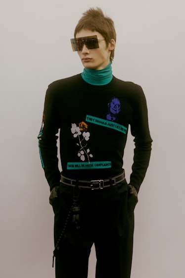 A model in a Dior black sweater with a flower and green text on it, looking to the side 