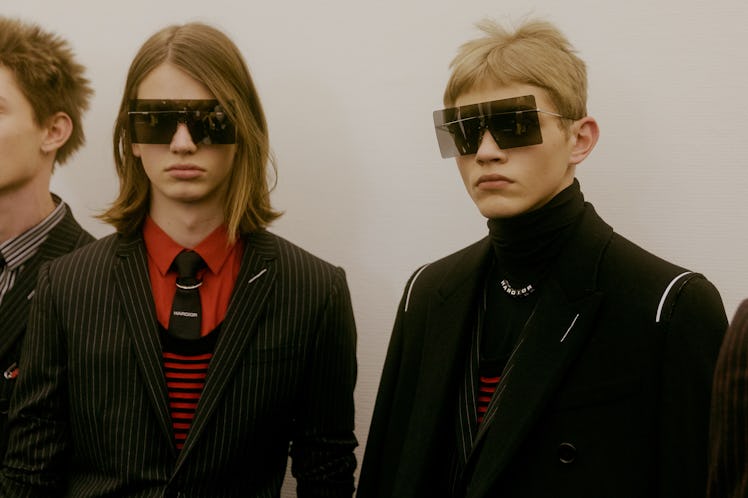 Two models at the Dior Homme Fall 2017 show wearing large square sunglasses and black suits 