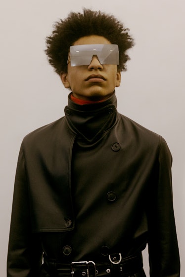 A model in a leather black Dior trench coat with a high collar and large, square-shaped sunglasses 