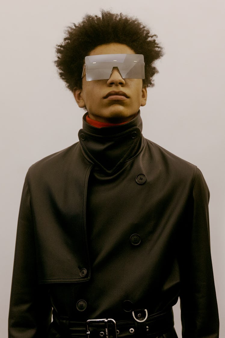 A model in a leather black Dior trench coat with a high collar and large, square-shaped sunglasses 