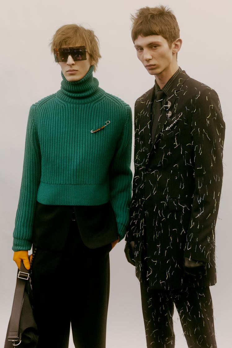 Two models in a green Dior turtleneck and a black suit with white curvy lines on it 
