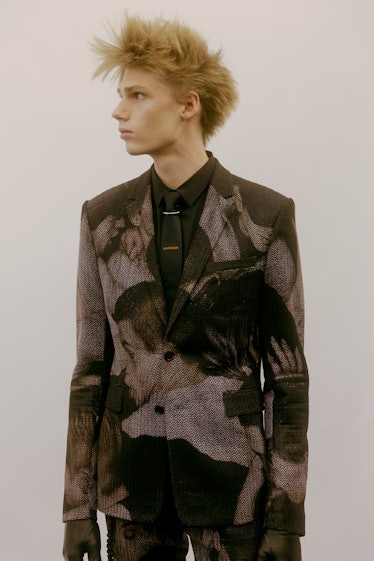 A model in a black Dior blazer with white illustrations of men on it 