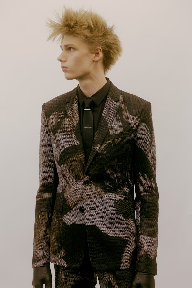 A model in a black Dior blazer with white illustrations of men on it 