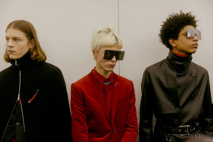 Three models lined up backstage at the Dior Homme Fall 2017 show in red and black outfits 