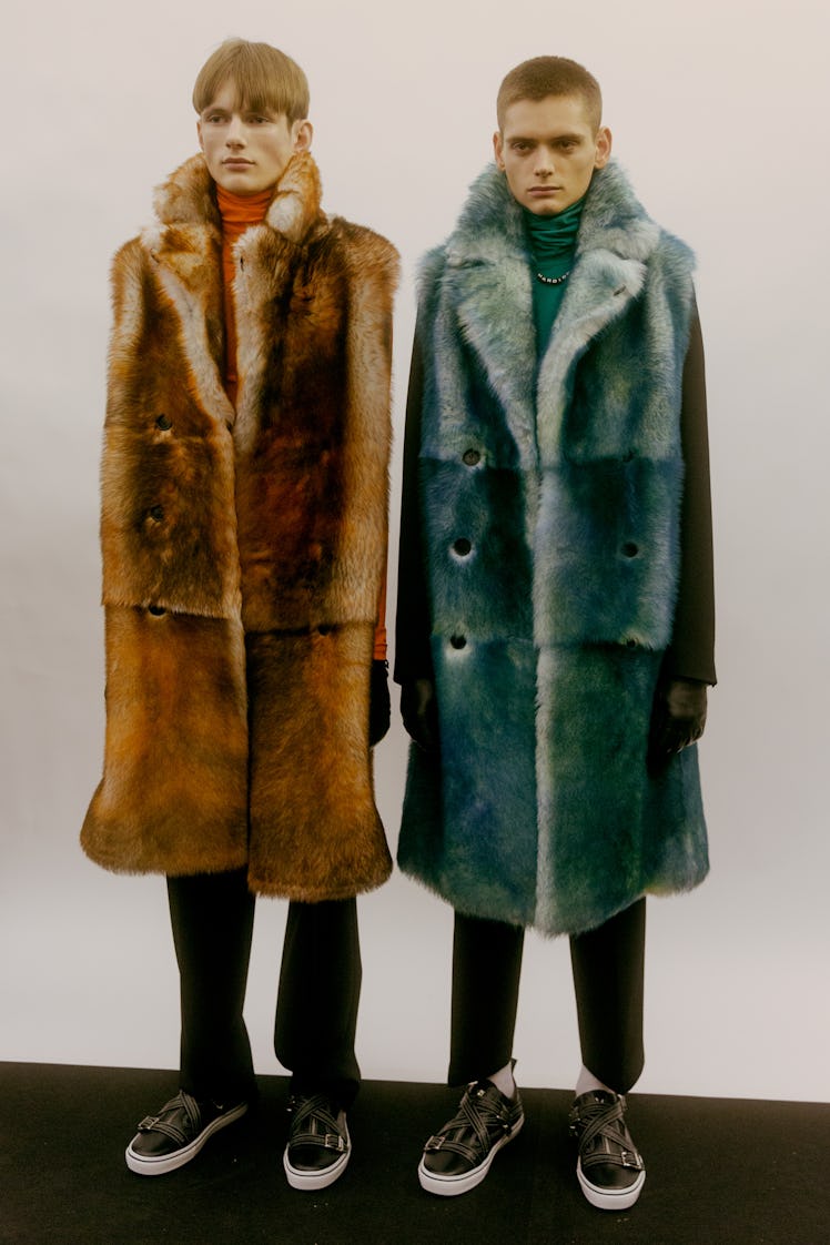 Two models at the Dior Homme Fall 2017 show in brown and blue long fur vests 