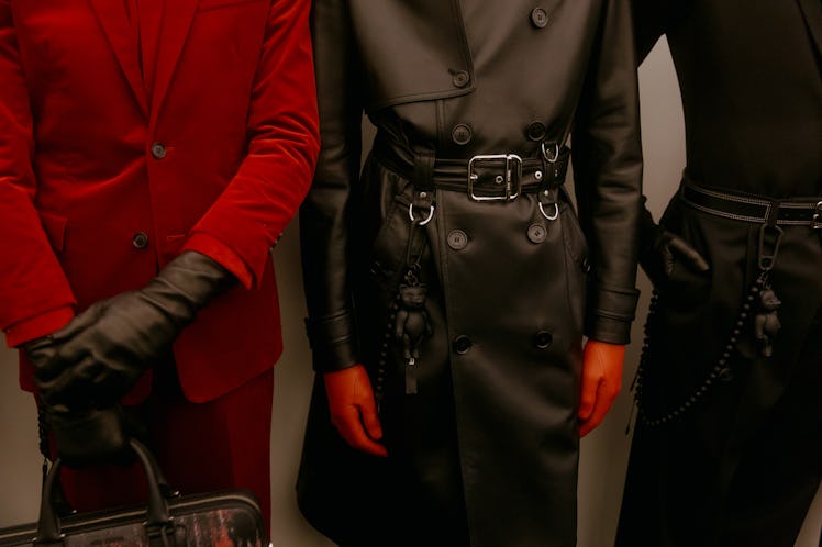 A model in a red Dior suit and black gloves standing next to a model in a black leather trench coat ...