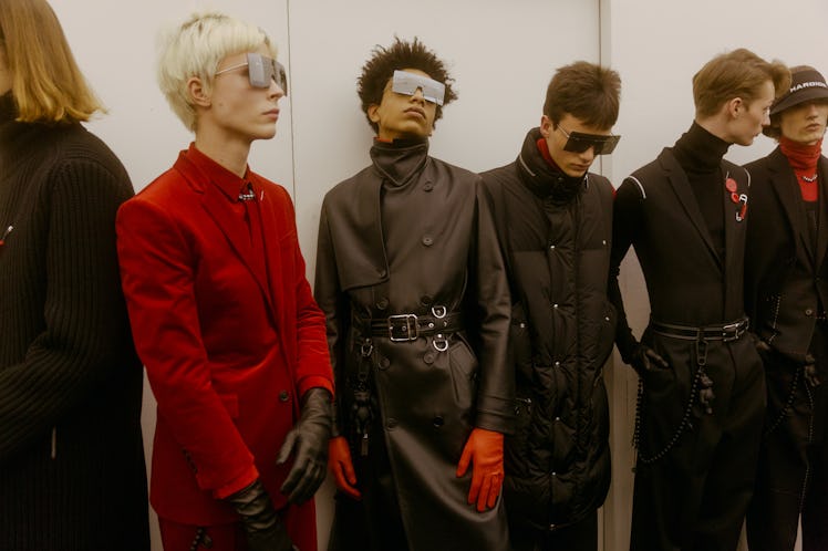 Models lining up backstage at the Dior show, wearing large squared sunglasses and looking in various...