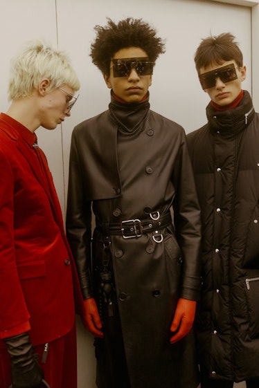 A model in a red suit, a model in a leather black trench coat and a model in a black puffer coat sta...