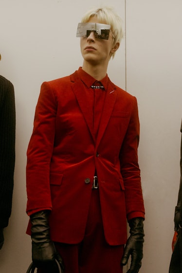 A model in a red suit with a red button-up underneath, looking into the distance at the Dior Homme F...