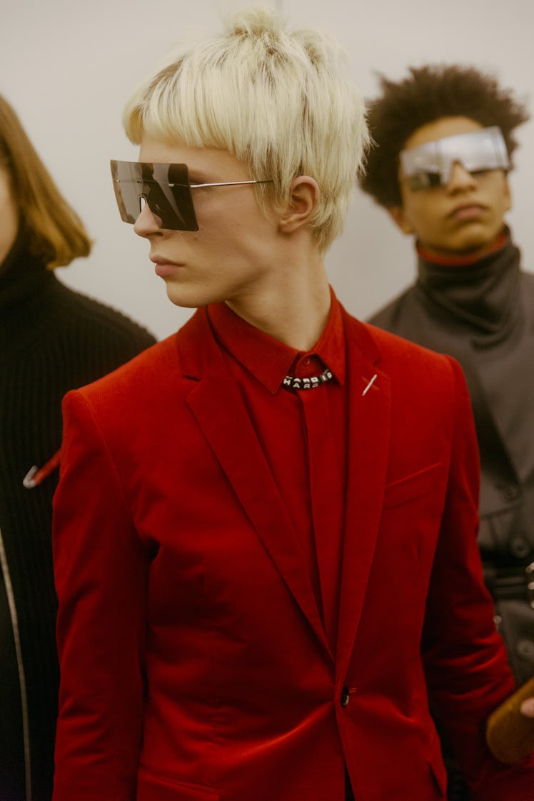 A model backstage at the Dior Homme Fall 2017 show in a red suit, red button-up and large square sun...
