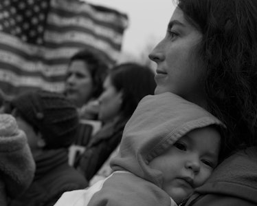 A woman holding her child and a group of people holding the American flag at the Women’s March in Wa...
