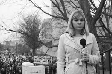 A news reporter in a coat holding a microphone with a crowd gathered behind her at the Women's March...