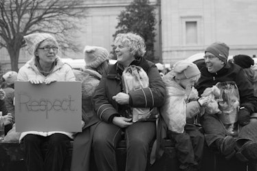 Three women and a man sitting on a bench with one woman holding a poster with the text 'RESPECT'