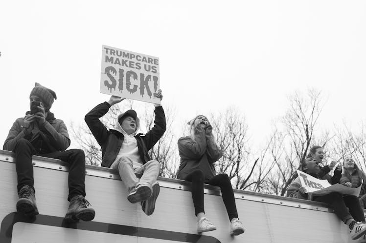 Five people sitting on top of a billboard and the poster 'Trumpcare makes us sick' at the Women's Ma...