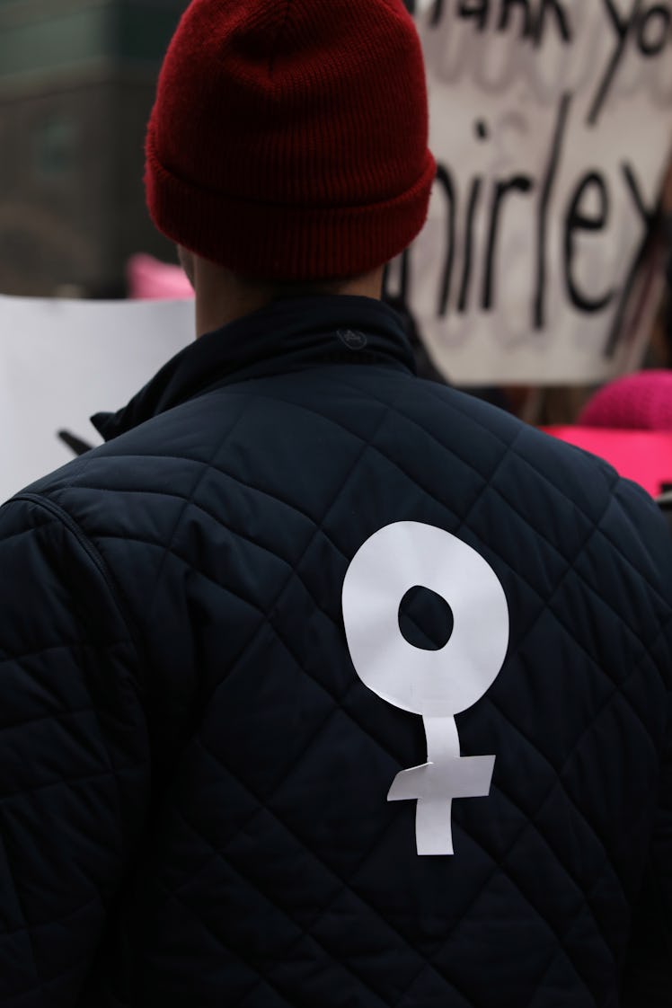A man in a black jacket and a red beanie with a white female symbol at the New York City Women’s Mar...