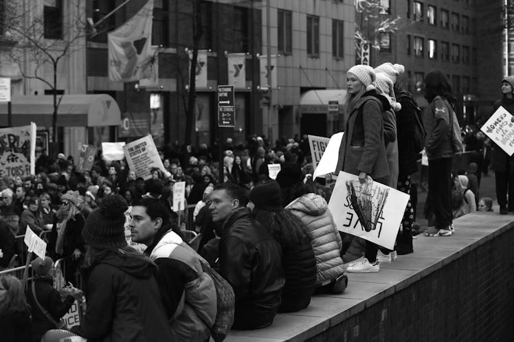 A group of people sitting on a wall and a large crowd in the background at the New York City Women's...