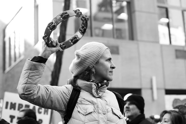 A woman n a jacket and beanie holding a tambourine at the New York City Women's March