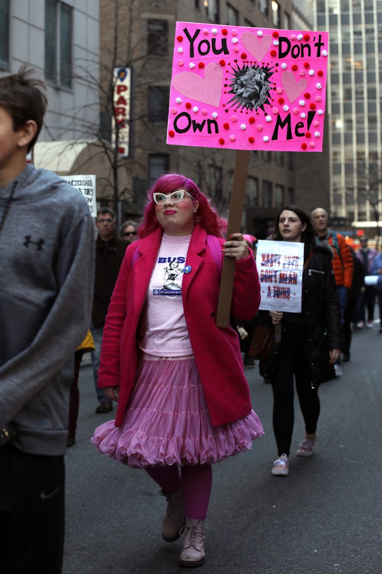 A woman in a red jacket and pink skirt holding a sign 'You don't own me!' at the New York City Women...