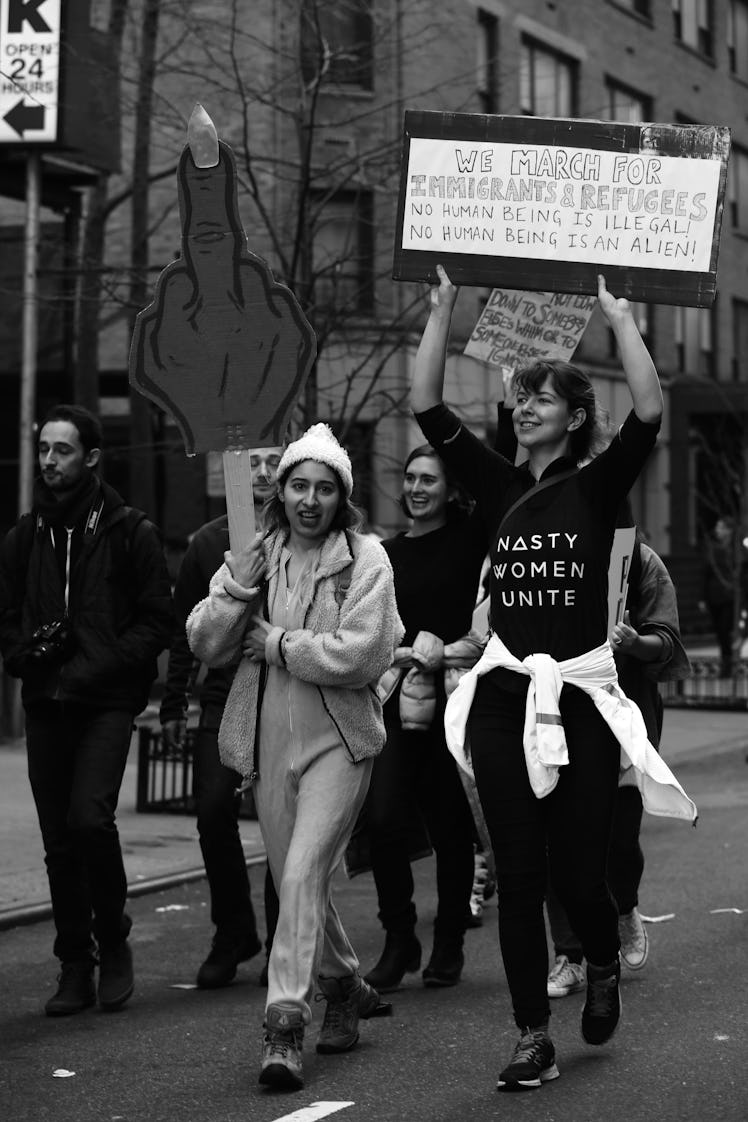 A woman holding a large middle finger sign and a woman holding a protest poster at the New York City...