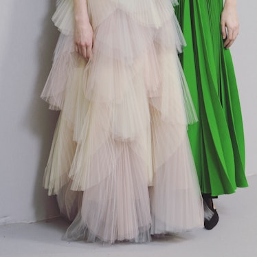 A model in a beige tulle gown next to a model wearing a green pleated dress