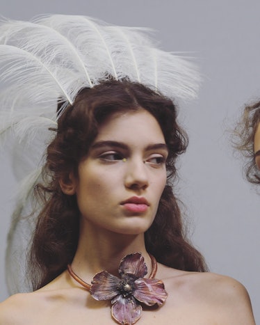 A model with a white feather crown and a flower necklace