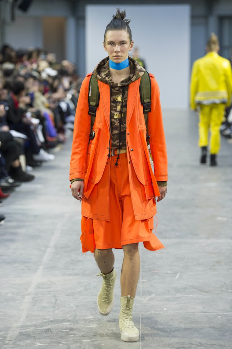 A model wearing an orange jacket and shorts, a blue choker, and carrying a backpack at the Sankuanz ...