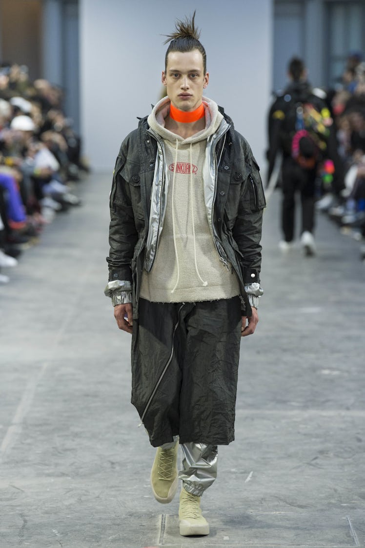 A model wearing a black jacket and pants with a gray hoodie beneath and an orange choker at the Sank...