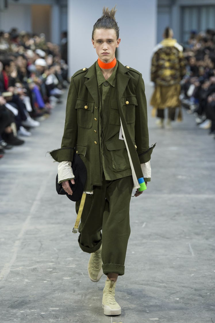 A model wearing navy green pants, and a navy green jacket with an orange choker at the Sankuanz Fall...