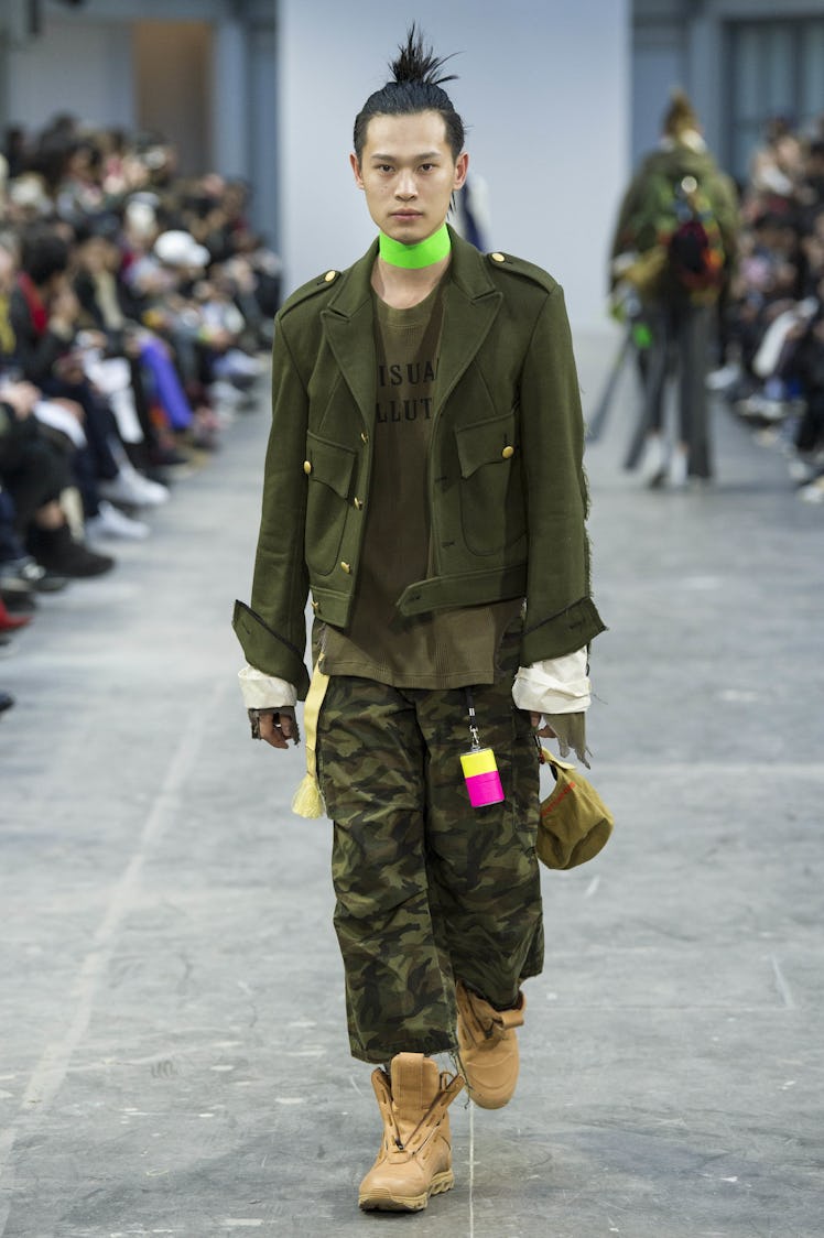 A model wearing camo pants, a navy green jacket, and a green choker at the Sankuanz Fall 2017 runway