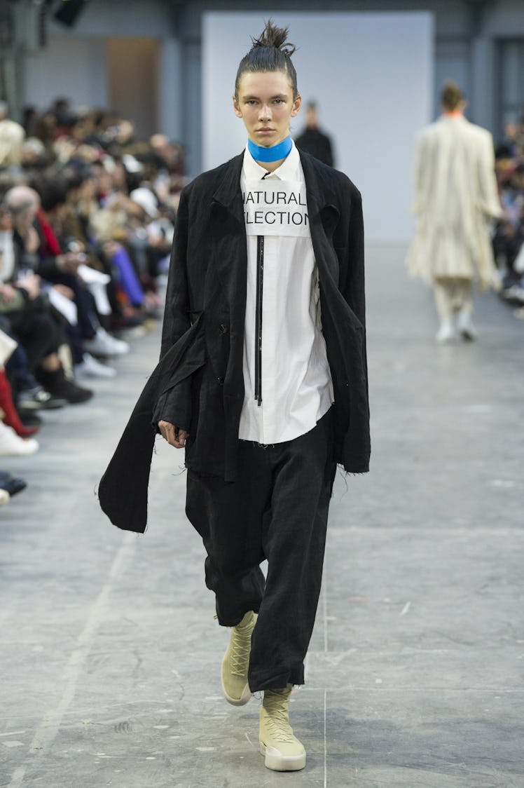 A model wearing black pants, a white shirt, a black jacket, and a blue choker at the Sankuanz Fall 2...