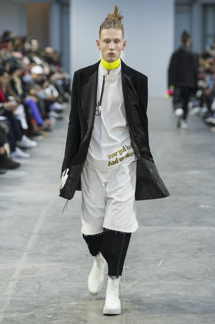 A model wearing black and white pants, a white shirt, a long black blazer, and a yellow choker at th...