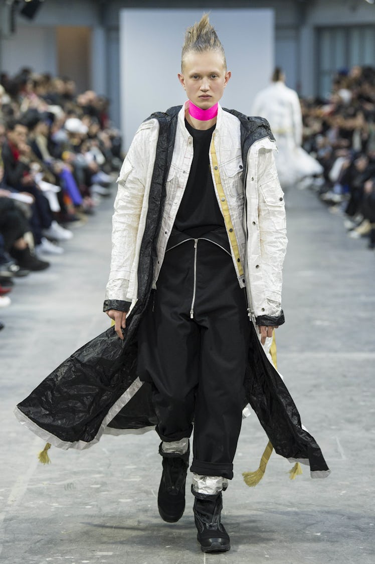 A model wearing a black jumpsuit with a long white jacket and a pink choker at the Sankuanz Fall 201...