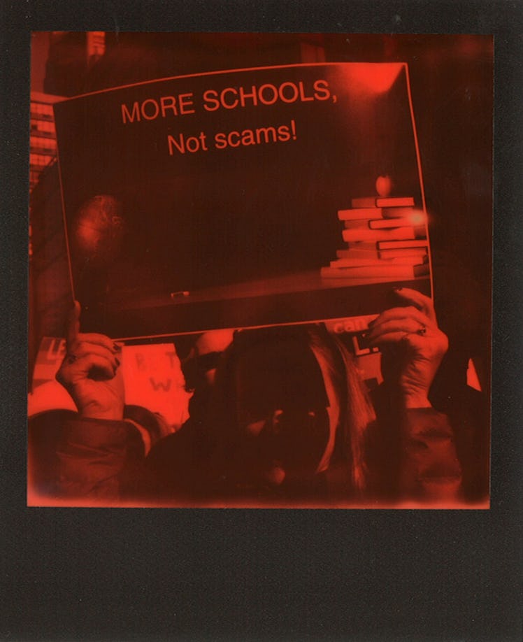 A woman holding a poster with "MORE SCHOOLS, Not scams" text at the Women’s March in NYC