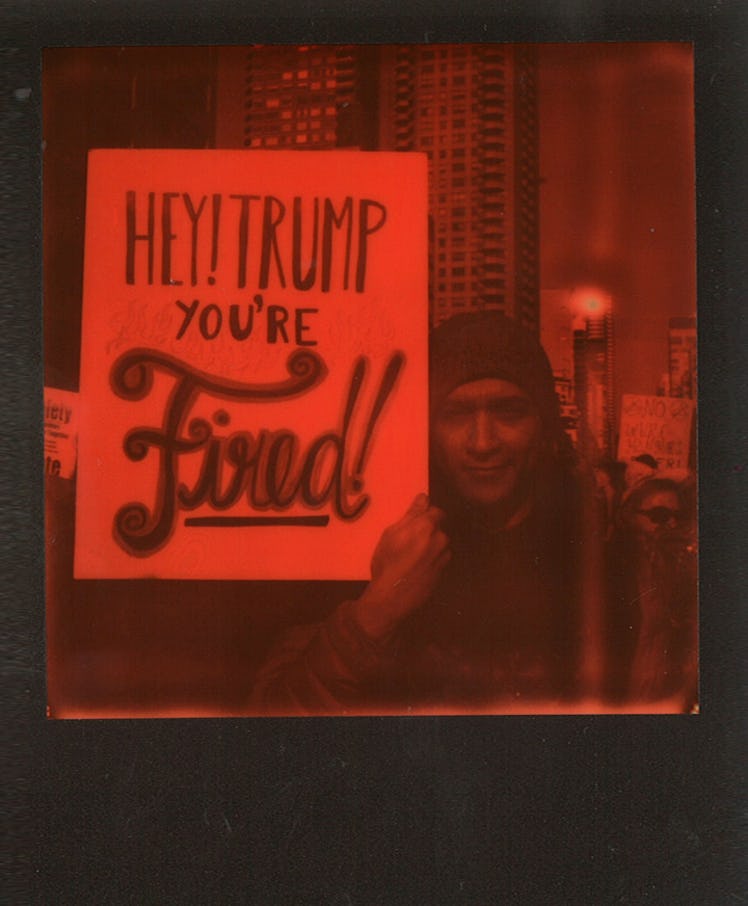 A man holding a poster with "HEY! TRUMP YOU'RE FIRED!" text at the Women’s March in NYC