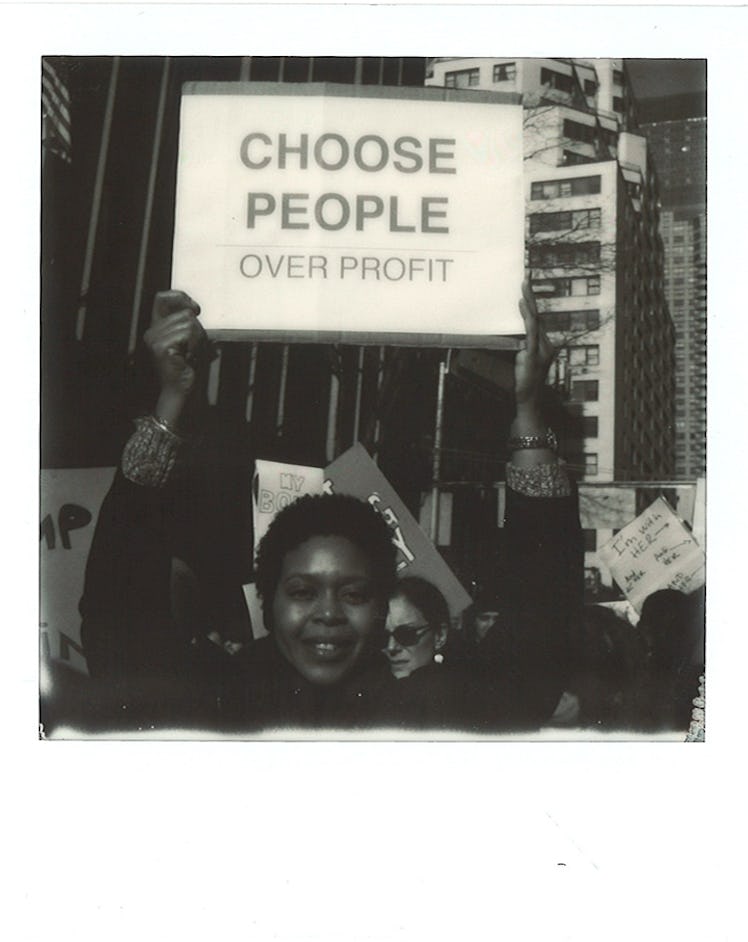 A woman holding a poster with "CHOOSE PEOPLE OVER PROFIT" text at the Women’s March in NYC