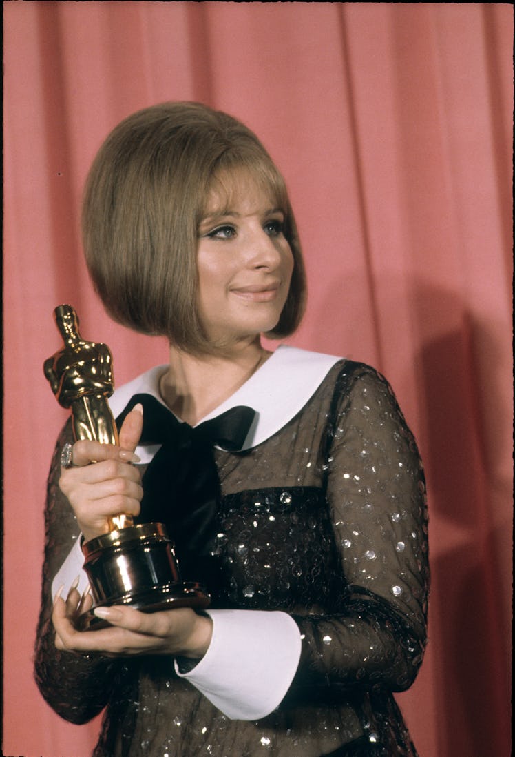 Barbra Streisand accepting an Oscar in a sheer, bedazzled black dress with a white collar and sleeve...